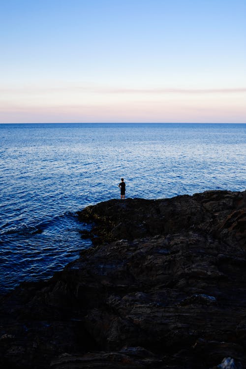 站在水体旁边的岩石上的人 · 免费素材图片