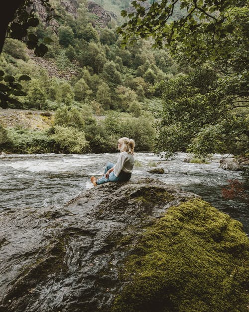 女人坐在河边的岩层附近 · 免费素材图片