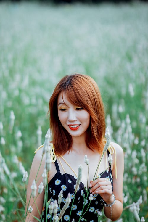 黑色的花顶独自站在草地上的微笑妇女的选择性焦点照片 · 免费素材图片
