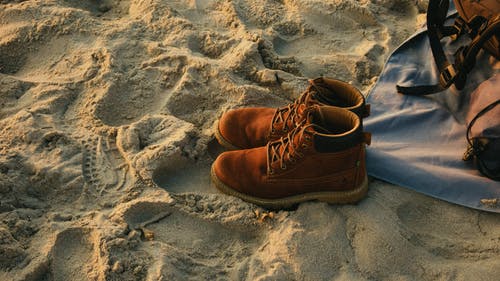双棕色工作靴在沙滩上 · 免费素材图片