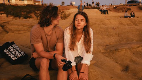 男人和女人坐在沙滩上的照片 · 免费素材图片