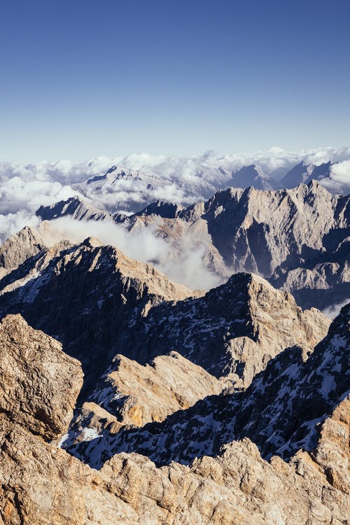 空中射击的棕色和灰色的岩石山脉，其斜坡上爬行的云层 · 免费素材图片