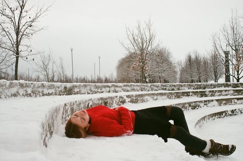穿红色毛衣躺在雪地上的女人 · 免费素材图片