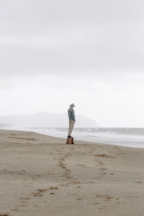 戴着帽子站在海边的人 · 免费素材图片