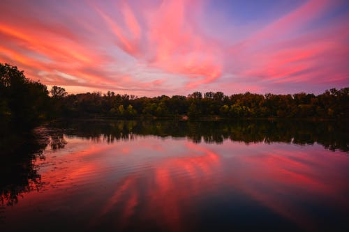 湖高高耸立，绿树成荫，橙色和蓝色的天空 · 免费素材图片