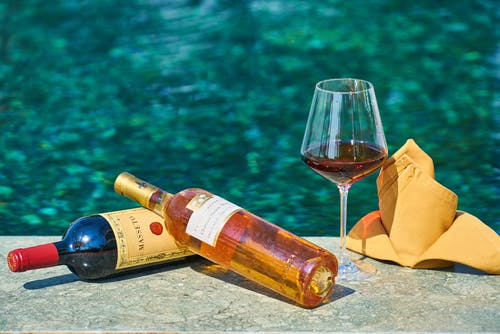 在游泳池旁的酒杯旁边的两个标签的瓶酒 · 免费素材图片