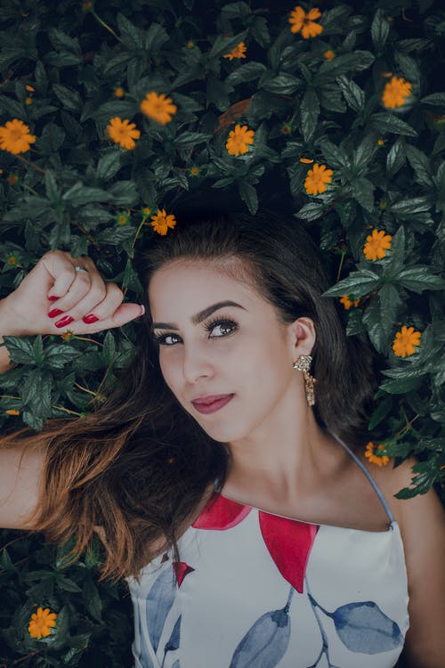 女人穿着白色，蓝色和红色的印花的上衣躺在床上黄色的花朵，绿色的叶子 · 免费素材图片