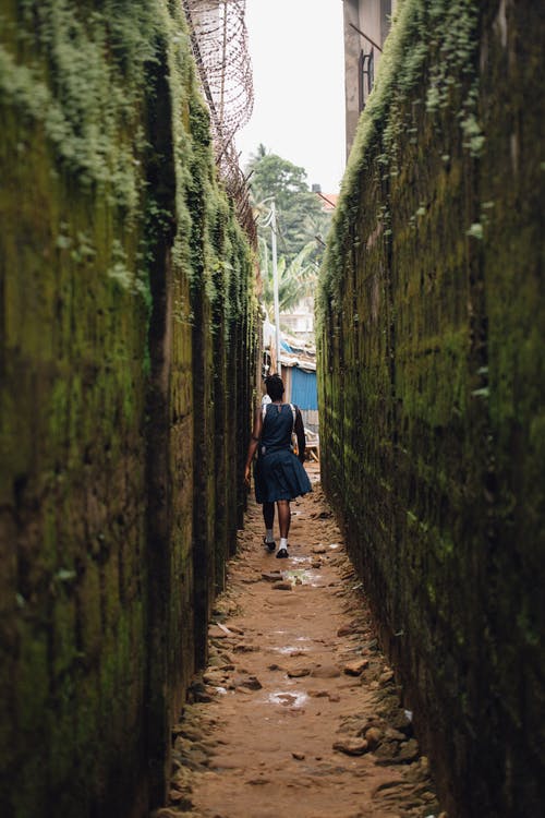 女人走在混凝土墙之间的小巷 · 免费素材图片
