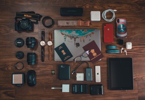 棕色木质表面上的护照，照相机，电池充电器，手表和电缆 · 免费素材图片
