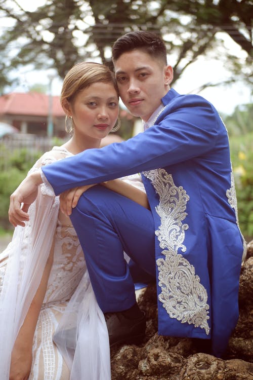 蓝色西装的男人坐在白色婚纱礼服的女人面前的岩石上 · 免费素材图片