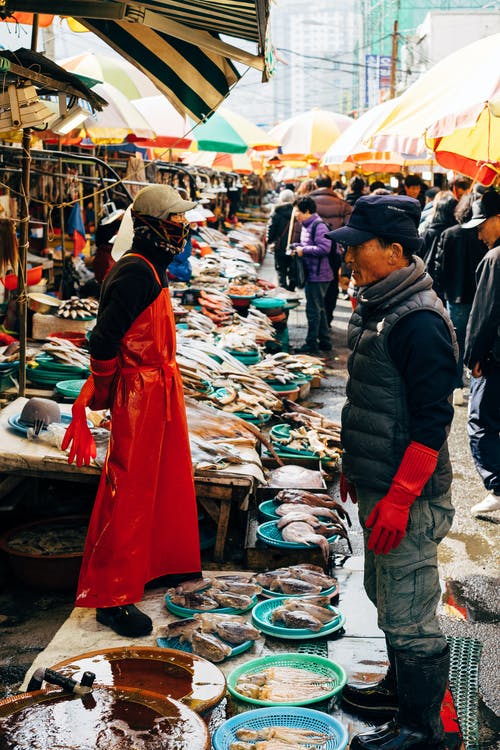 一群人在鱼市场里衬着五颜六色的雨伞 · 免费素材图片