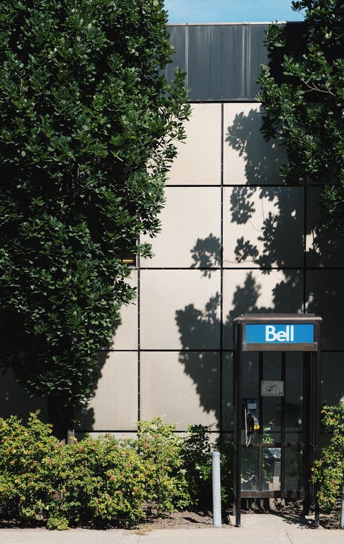 绿叶树旁的白色混凝土建筑附近的电话亭 · 免费素材图片