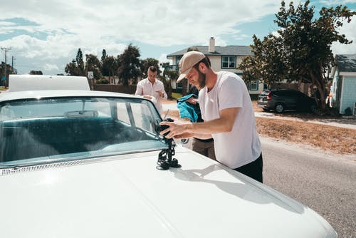 男子身穿白色圆领t恤，拿着相机在白色车辆上 · 免费素材图片