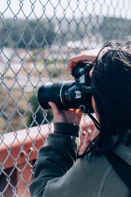 女人拿着单反相机在铁丝网栅栏后面拍照 · 免费素材图片