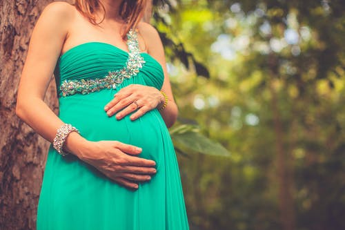 孕妇在绿色的单肩连衣裙，抱着她的肚子 · 免费素材图片