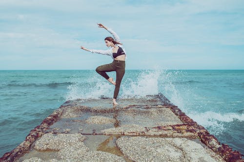 女人做防波堤上波溅背后的防波堤上的芭蕾舞姿势 · 免费素材图片