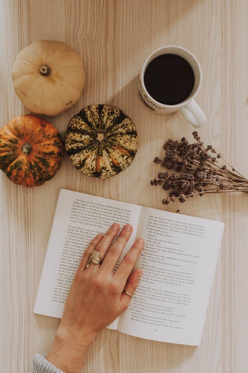 一个女人的手在桌上的咖啡杯旁边的书上的顶视图 · 免费素材图片