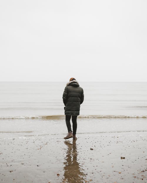 一个人穿着黑色泡泡夹克走向大海的背影 · 免费素材图片
