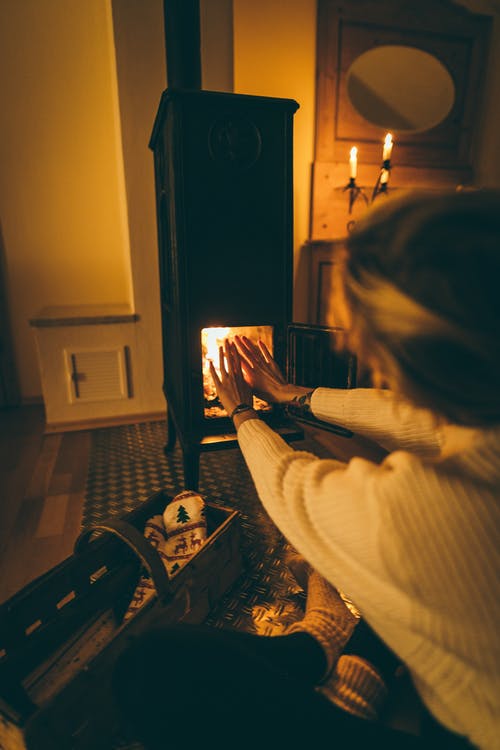 女人穿着白色的长袖试图在壁炉上发热 · 免费素材图片