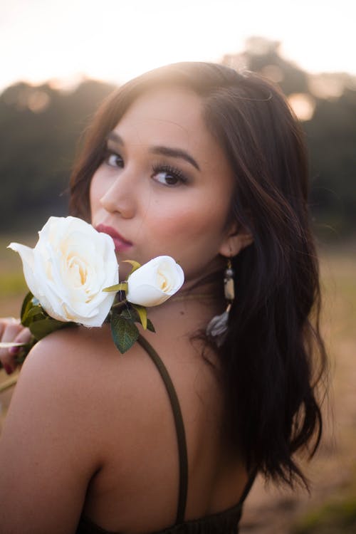 女人拿着白色的玫瑰花摆姿势的选择性焦点照片 · 免费素材图片