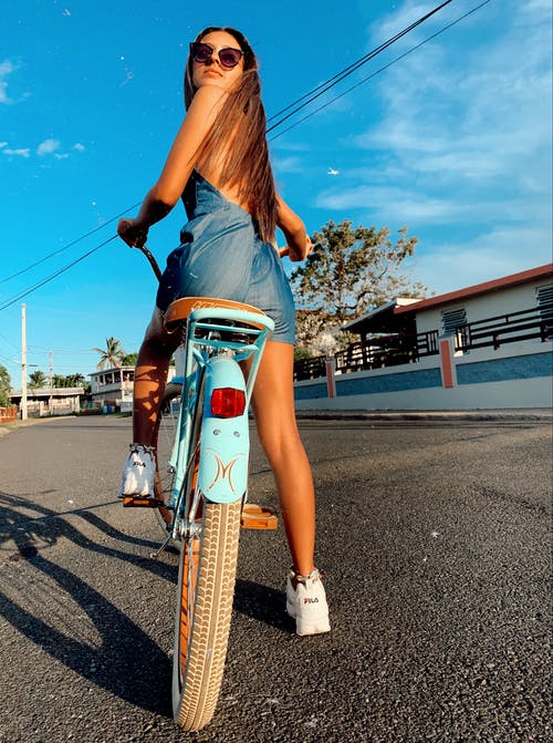 后视图的女人在蓝色的裙子和太阳镜坐在蓝色的自行车回望的照片 · 免费素材图片