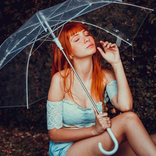 女人闭着眼睛坐在一把透明的雨伞时坐着的照片 · 免费素材图片