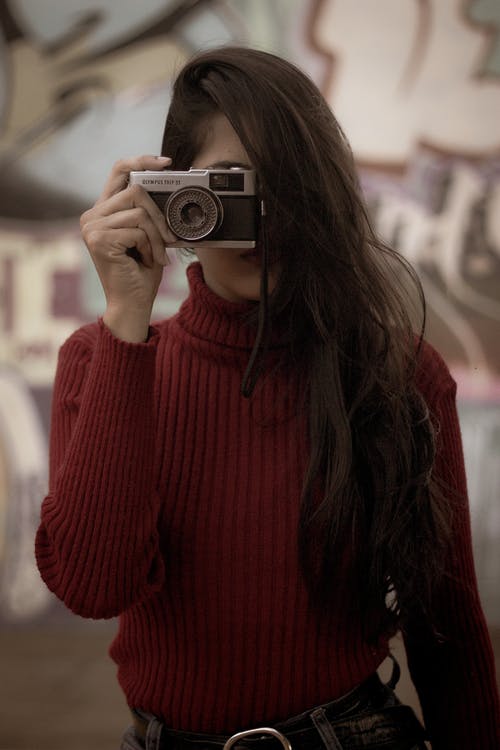 拿着胶片相机的红色拉脖子毛衣的女人的选择性聚焦照片 · 免费素材图片