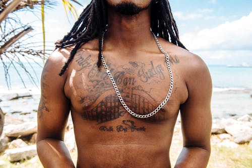 胸的男人与纹身在海滩上摆姿势的特写照片 · 免费素材图片