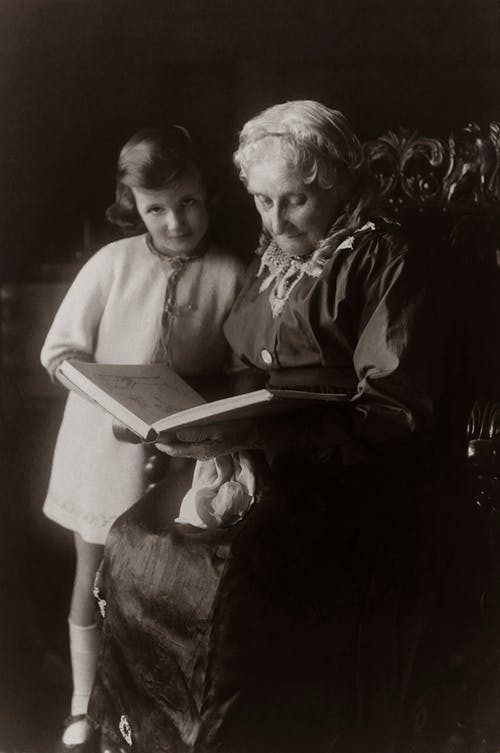 读一本书时坐在椅子上附近女孩的老女人 · 免费素材图片
