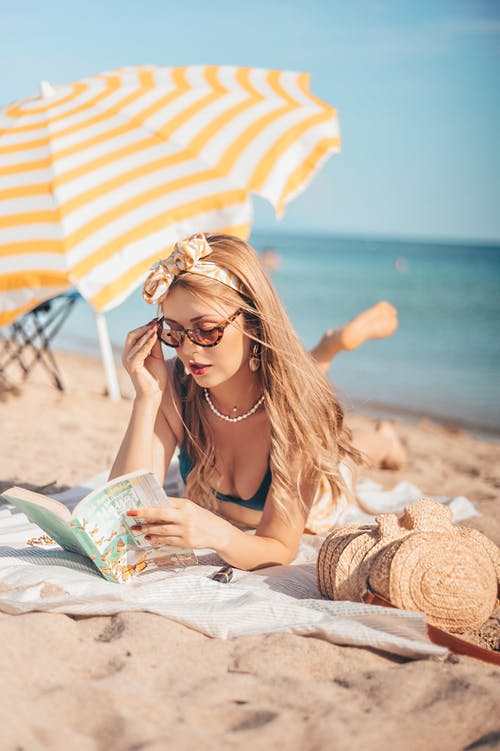 妇女躺在沙滩上看书 · 免费素材图片