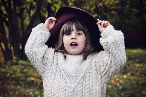 褐红色的帽子和白色针织的毛衣摆姿势的小女孩的选择重点 · 免费素材图片