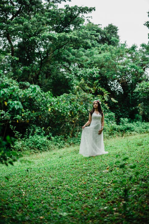 抬头独自一人站在草地上的白色礼服和花冠的女人的照片 · 免费素材图片