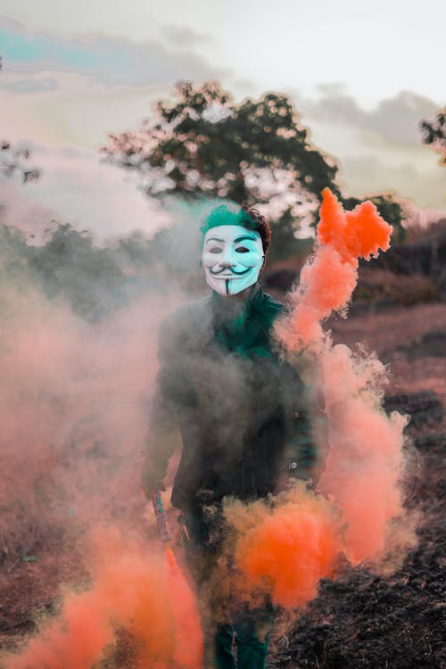 人戴着盖伊·福克斯面具包围彩色烟雾 · 免费素材图片