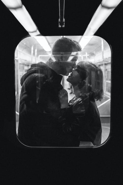 男人站在火车里亲吻女人的鼻子的灰度照片 · 免费素材图片