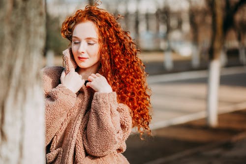穿着棕色羊毛大衣的长卷发红头发女人 · 免费素材图片