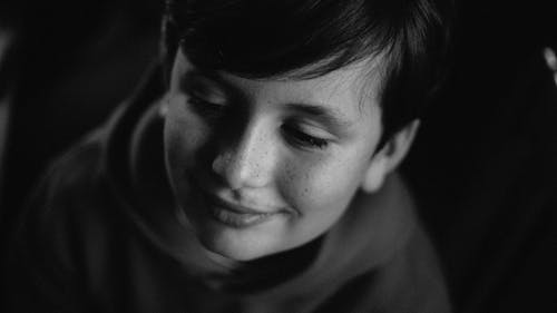 微笑的男孩在一个黑暗的房间里看着别处的灰度照片 · 免费素材图片