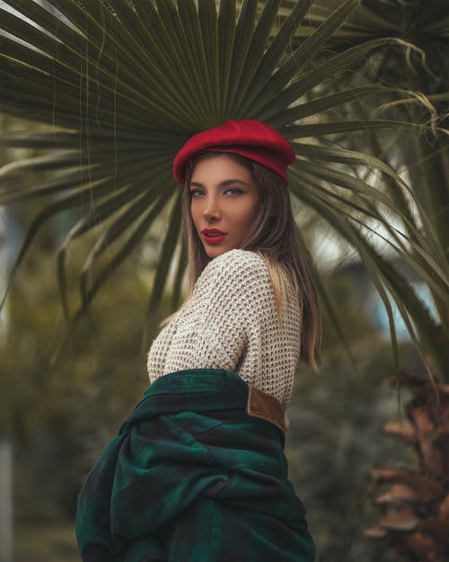 在棕榈树的叶子下摆姿势的红色帽子的女人的选择性聚焦照片 · 免费素材图片