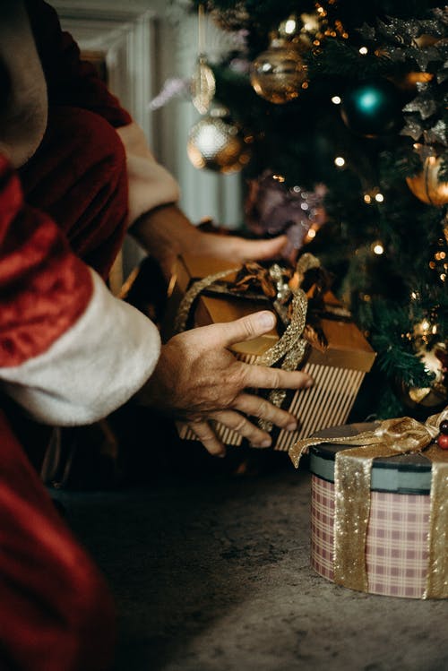 穿着圣诞老人服装的人拿着金礼物盒 · 免费素材图片