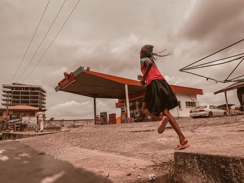 女人跑在红色和白色的加油站附近 · 免费素材图片