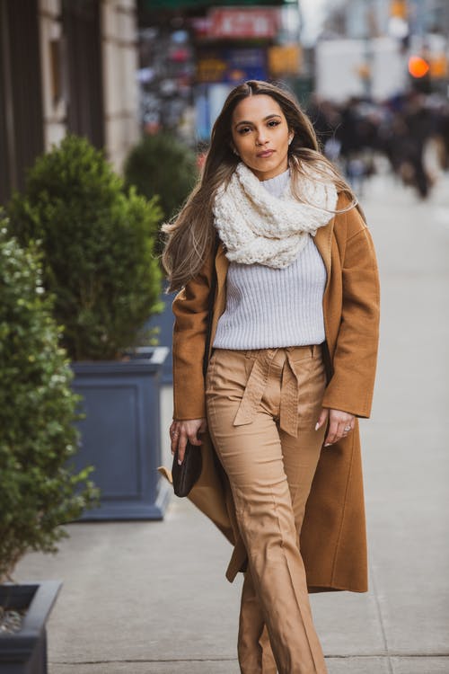 一个女人穿着棕色大衣和裤子在人行道上行走的选择性焦点 · 免费素材图片