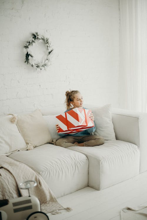 女孩坐在白色的沙发上，她的双腿交叉持有本的照片 · 免费素材图片