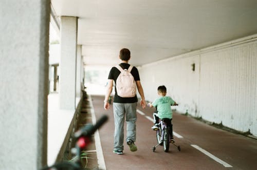 在男孩骑自行车旁边行走的人 · 免费素材图片
