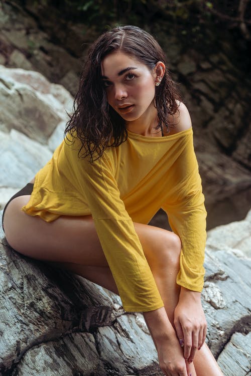女人坐在岩石上穿黄色船员的脖子t恤 · 免费素材图片