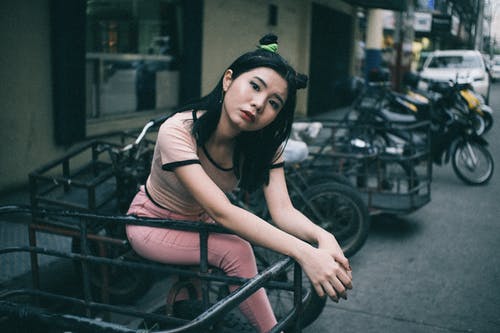 年轻女子坐在马路边的一辆停放的摩托车 · 免费素材图片