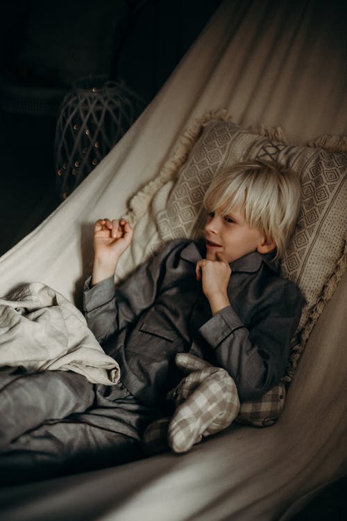 男孩穿着灰色衣领纽扣式长袖衬衫躺在床上 · 免费素材图片