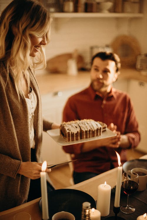 女人站在服务切片的蛋糕和男人坐在桌子旁边 · 免费素材图片
