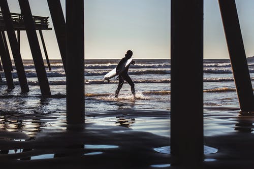 冲浪者走在海滩码头附近 · 免费素材图片