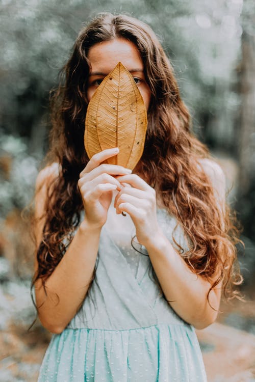 女人捂着脸与一片棕色的叶子 · 免费素材图片