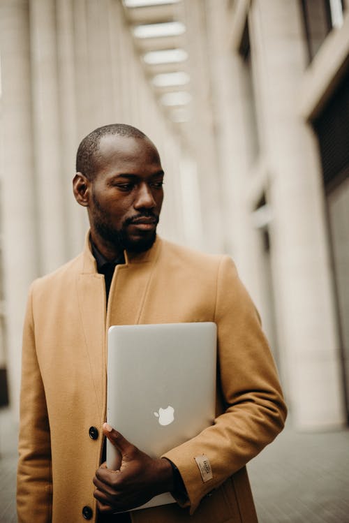 男人穿着棕色外套拿着mac的书 · 免费素材图片