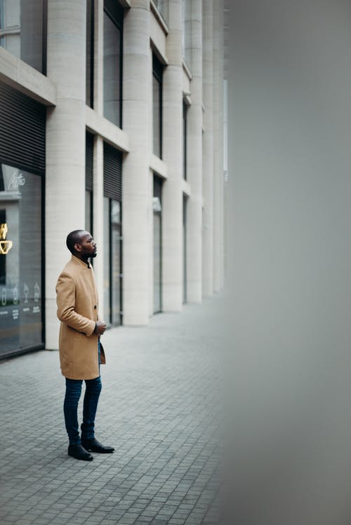 在建筑物外摆姿势的棕色外套的男人的侧视图照片 · 免费素材图片